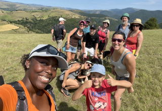 Gruppe von Menschen wandert und lächelt im Sonnenschein bei Flower Camping Le Pont du Tarn in Occitanie, Frankreich.