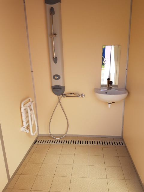Rolstoeltoegankelijke badkamer met douche, opklapbaar zitje, lavabo en spiegel in een vakantiepark.