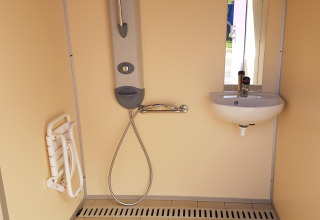 Rolstoeltoegankelijke badkamer met douche, opklapbaar zitje, lavabo en spiegel in een vakantiepark.