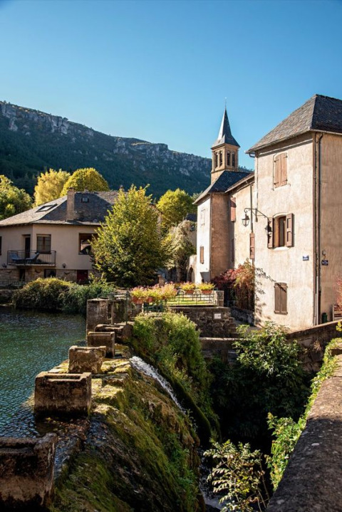 Malerisches Dorf bei Florac-Trois-Rivières in Okzitanien, Frankreich, mit Fluss, Häusern und Bergen.