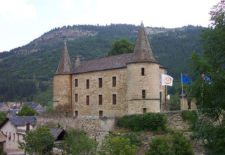 Stone castle with towers set against hillsides at Flower Camping Le Pont du Tarn in Occitanie, France.