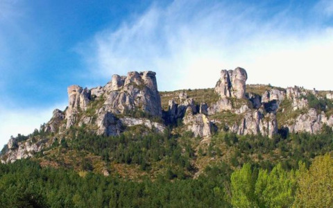 Rocky cliffs and green hills near Florac-Trois-Rivières in Occitanie, France, beneath a blue sky.