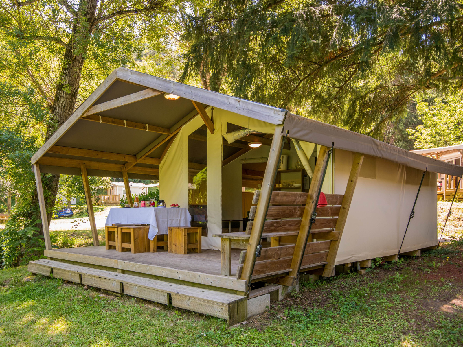 Freeflower Comfort safaritent met houten veranda en eethoek, gelegen tussen groene bomen in de natuur.