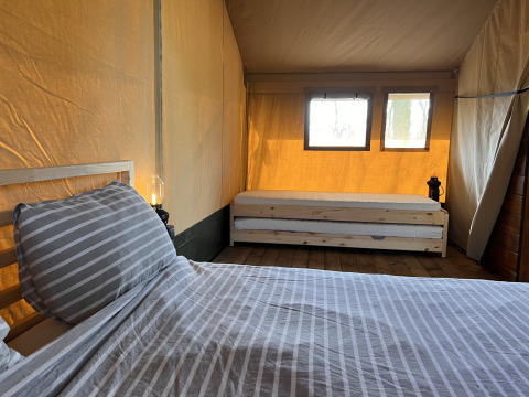 Intérieur d'une tente safari avec deux lits, plancher en bois et fenêtres laissant entrer la lumière.