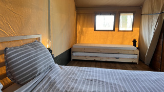 Intérieur d'une tente safari avec deux lits, plancher en bois et fenêtres laissant entrer la lumière.