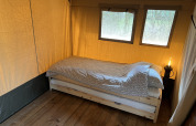 A simple bed inside a safari tent at Camping 'de Val' in the Netherlands, with wood flooring and sunlight.