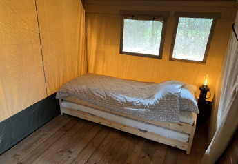 A simple bed inside a safari tent at Camping 'de Val' in the Netherlands, with wood flooring and sunlight.