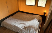 Interior view of a safari tent with a double bed and bedside lamp at Camping 'de Val' in the Netherlands.