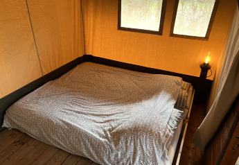 Vista interior de una tienda safari con cama doble y lámpara junto a la cama en Camping 'de Val', Países Bajos.