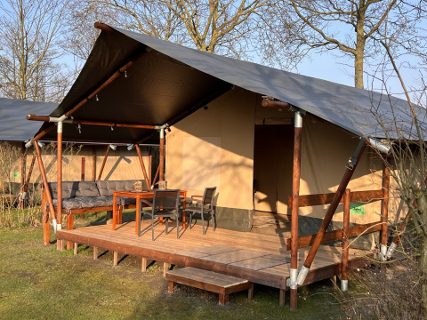 Safari tent at Camping 'de Val' in the Netherlands with wooden porch, outdoor seating, and garden furniture.