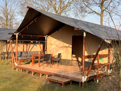 Tienda safari en Camping 'de Val', Países Bajos, con porche de madera y muebles de jardín al sol.