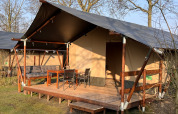 Safari tent at Camping 'de Val' in the Netherlands with wooden porch, outdoor seating, and garden furniture.