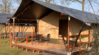 Safaritent bij Camping 'de Val' in Nederland, met houten terras, tuinmeubilair en gezellige zithoek.