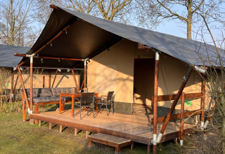 Safari-telt ved Camping 'de Val' i Holland med træveranda, havemøbler og udendørs siddeplads i solen.