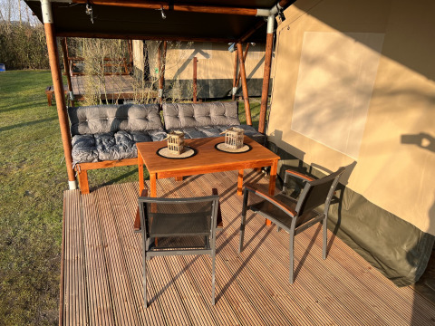 Udendørs siddeområde ved safaritelt på Camping 'de Val' i Holland med bord, stole og sofa.