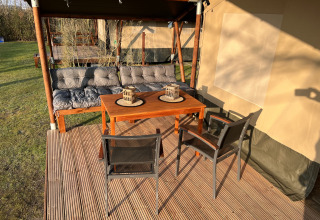 Outdoor seating area at safari tent at Camping 'de Val', Netherlands, with table, chairs, and a sofa bench.