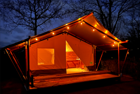 Verlichte safaritent op Camping ‘de Val’ in Nederland, sfeervol verlicht tijdens de nacht.
