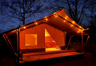 Beleuchtetes Safarizelt auf Camping 'de Val' in den Niederlanden bei Nacht mit Holzrahmen.