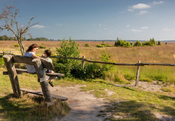 Eine Mutter und ihr Sohn sitzen auf einer Bank an einer Glamping-Unterkunft mit Blick auf die Wiese.