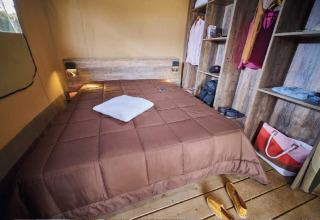 Innenansicht einer Safari-Lodge im Flower Camping Le Pont du Tarn mit Doppelbett und Holzregalen.
