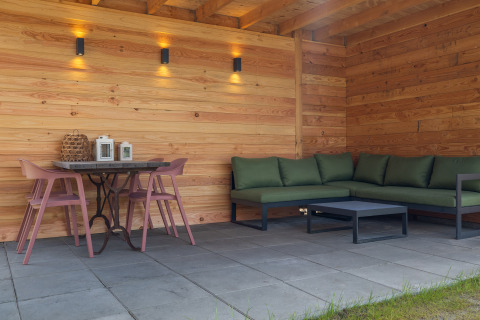 Overdekt terras van Forest villa «Heidehaas», De Kremmer, met groene hoekzetel en roze stoelen.