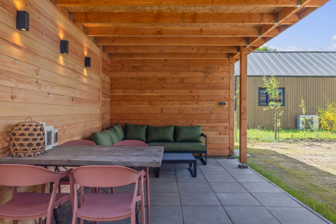 Overdekt houten terras aan Forest villa «Heidehaas» in De Kremmer, Nederland, met groene zetel.