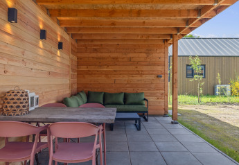 Overdekt houten terras aan Forest villa «Heidehaas» in De Kremmer, Nederland, met groene zetel.