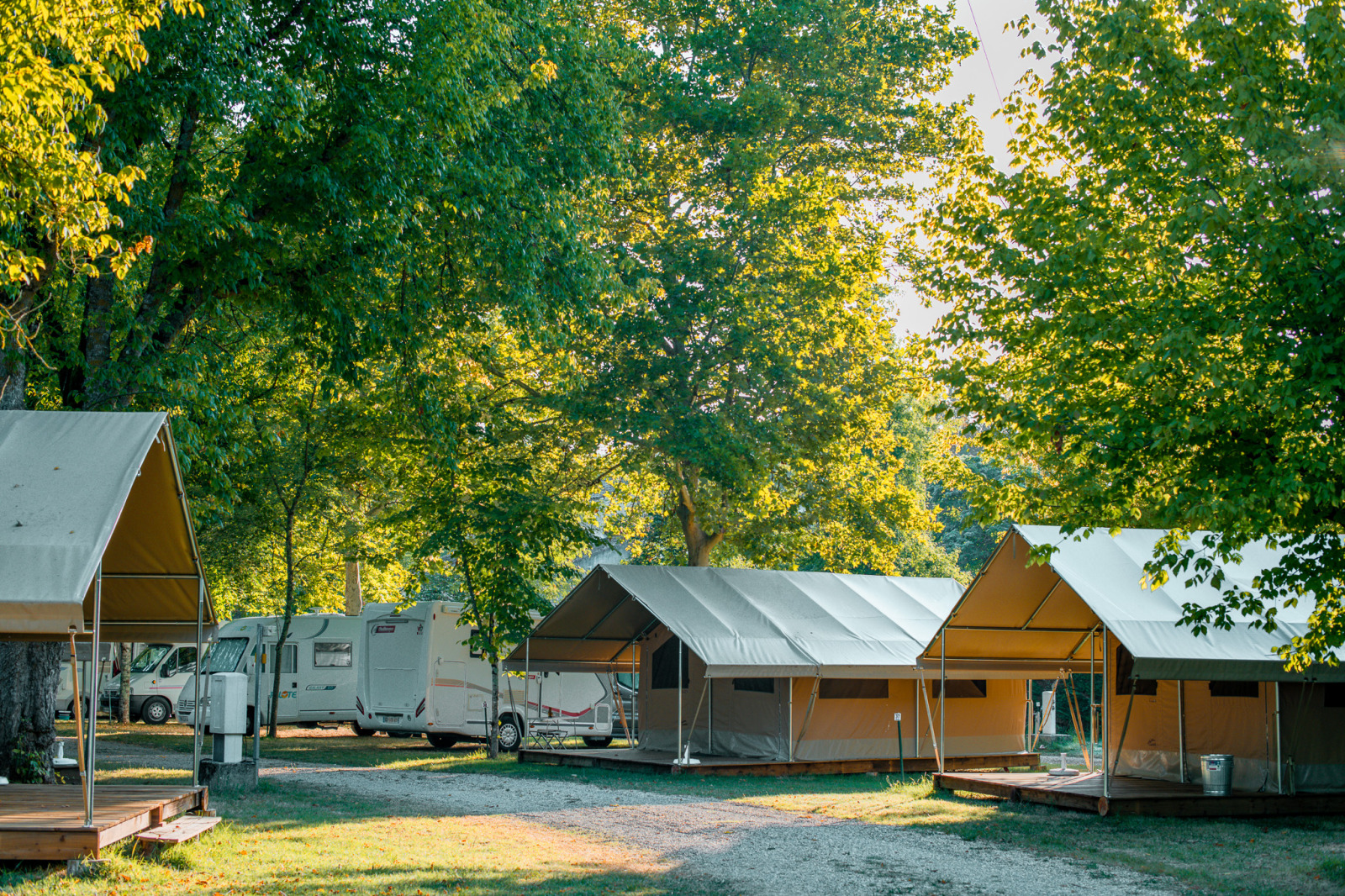 Safaritenten en campers tussen groene bomen bij Onlycamp Camping de l'Argenté, Frankrijk, in ochtendlicht.
