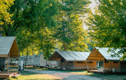 Safari-Zelte und Wohnmobile unter grünen Bäumen auf Onlycamp Camping de l'Argenté, Frankreich, am Morgen.