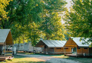 Tiendas safari y caravanas entre árboles verdes en Onlycamp Camping de l'Argenté, Francia, al amanecer.
