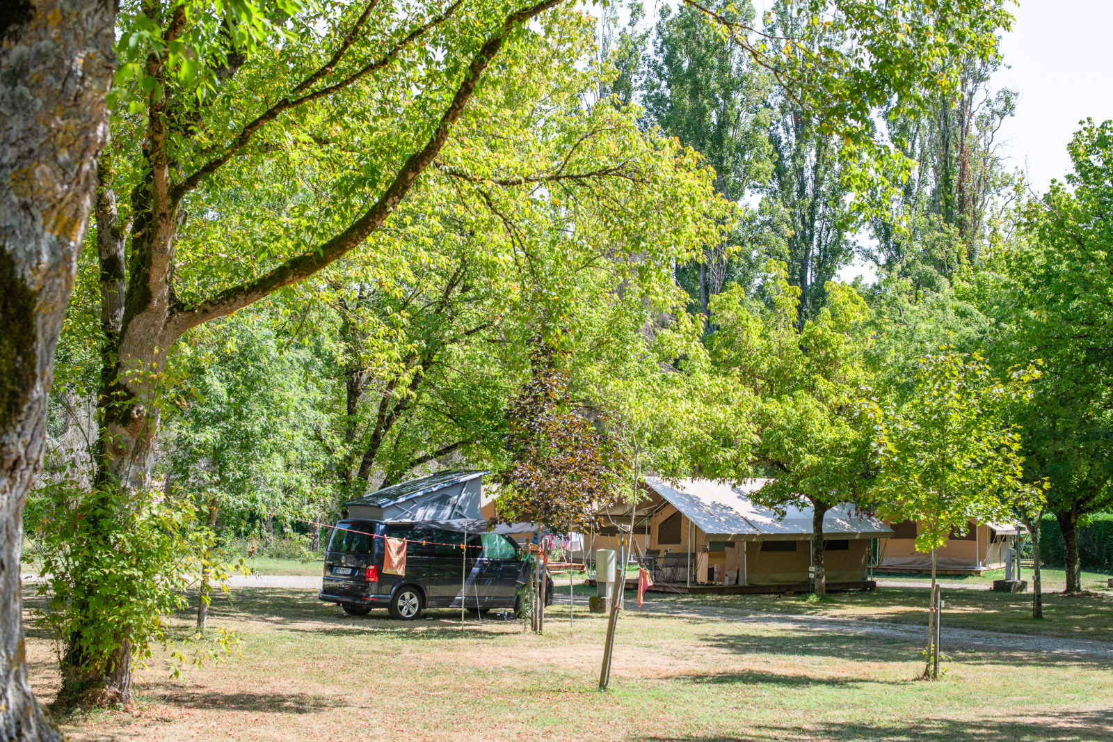 Safari Ponza-tent en camperbus tussen groene bomen bij Onlycamp Camping de l'Argenté in Frankrijk, rustige natuurcamping.