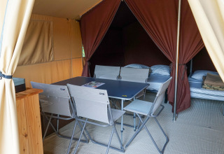 Interior de una tienda safari con mesa de comedor, sillas plegables y dos camas sobre suelo alfombrado.