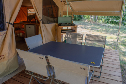 Coin repas extérieur sous tente safari avec table, chaises, réchaud et vue sur la nature environnante.