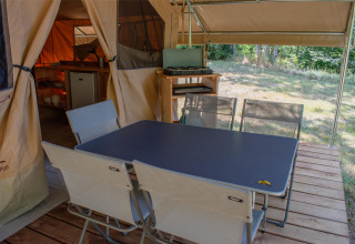 Coin repas extérieur sous tente safari avec table, chaises, réchaud et vue sur la nature environnante.