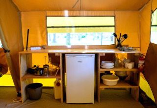 Zona de cocina dentro de una tienda safari con frigorífico pequeño, utensilios, vajilla y extintor.