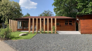 Moderne Holzlodge namens Private Lodge mit Kiesauffahrt, grünem Rasen und Holzpfosten am Eingang.