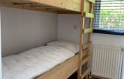 Holzetagenbett mit weißer Bettdecke in heller Lodge, neben Fenster und Heizung im Verscholen Dorp.