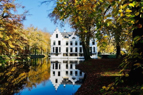 Wit gebouw aan het meer tussen herfstbomen, zoals gezien vanuit een glampingaccommodatie.