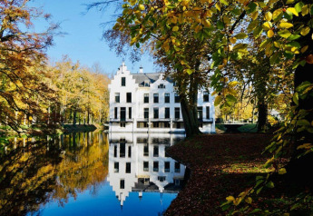 Smuk hvid bygning ved søen, omgivet af efterårstræer, set fra et glampingsted i naturskønne omgivelser.