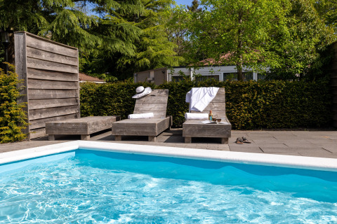 Zona piscina all'aperto con due lettini in legno, asciugamani e verde in una sistemazione glamping.