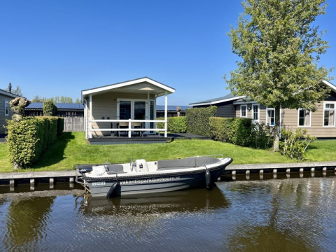 Lyst lodge ved vandet med båd og grøn have, beliggende i Meerkoet 4, Giethoorn, Holland, på en solrig dag.
