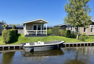 Lyst lodge ved vandet med båd og grøn have, beliggende i Meerkoet 4, Giethoorn, Holland, på en solrig dag.