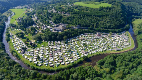 Luchtfoto van een luxe glampinglocatie omringd door groene heuvels en een kronkelende rivier in het landschap.