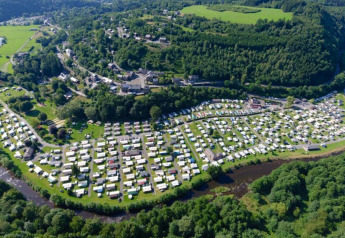 Vue aérienne d’un site de glamping luxueux entouré de collines verdoyantes et d’une rivière sinueuse.