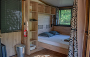 Gezellig ingerichte safaritent met dubbel bed, houten legplanken, grote ramen en stijlvolle gordijnen.