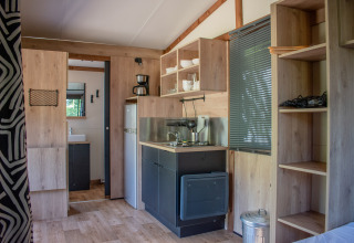 Interior de una tienda safari con cocina compacta, estantes abiertos, nevera y vista al baño.