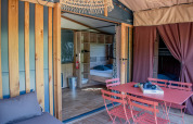 Safari-Zelt-Innenraum mit modernem Essbereich, Holzmöbeln sowie einem Schlafzimmer mit Doppelbett.
