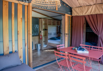 Interno di tenda safari con arredamento moderno, tavolo da pranzo rosso e zona notte con letto doppio.