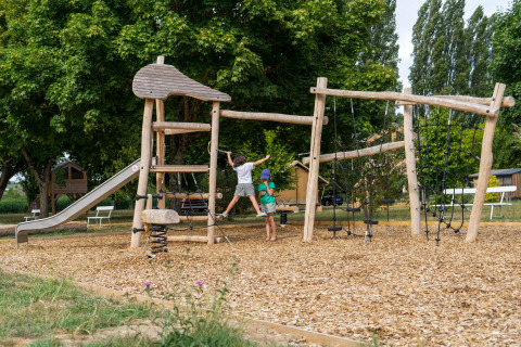 Niños juegan en un parque infantil de madera natural con tobogán en Onlycamp Camping La Gâtine.