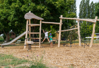 Des enfants jouent sur une aire de jeux en bois naturel avec toboggan au camping Onlycamp La Gâtine.